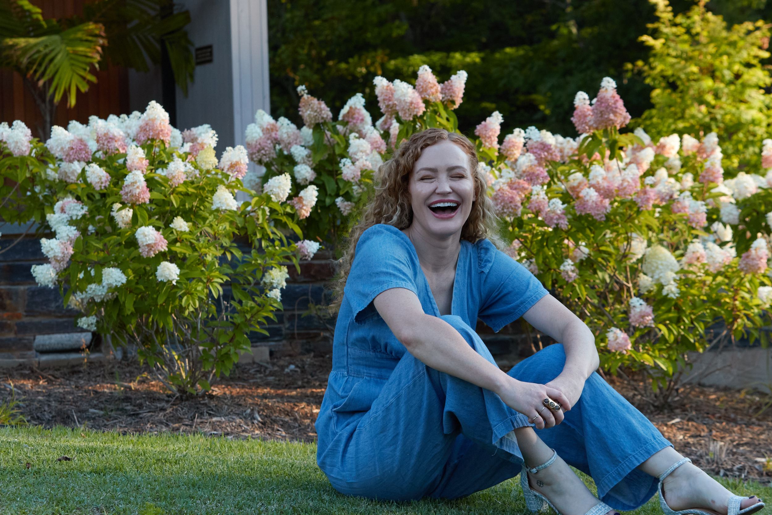 Carrie Davidson laughing on the grass in front of pink and white hydrangeas