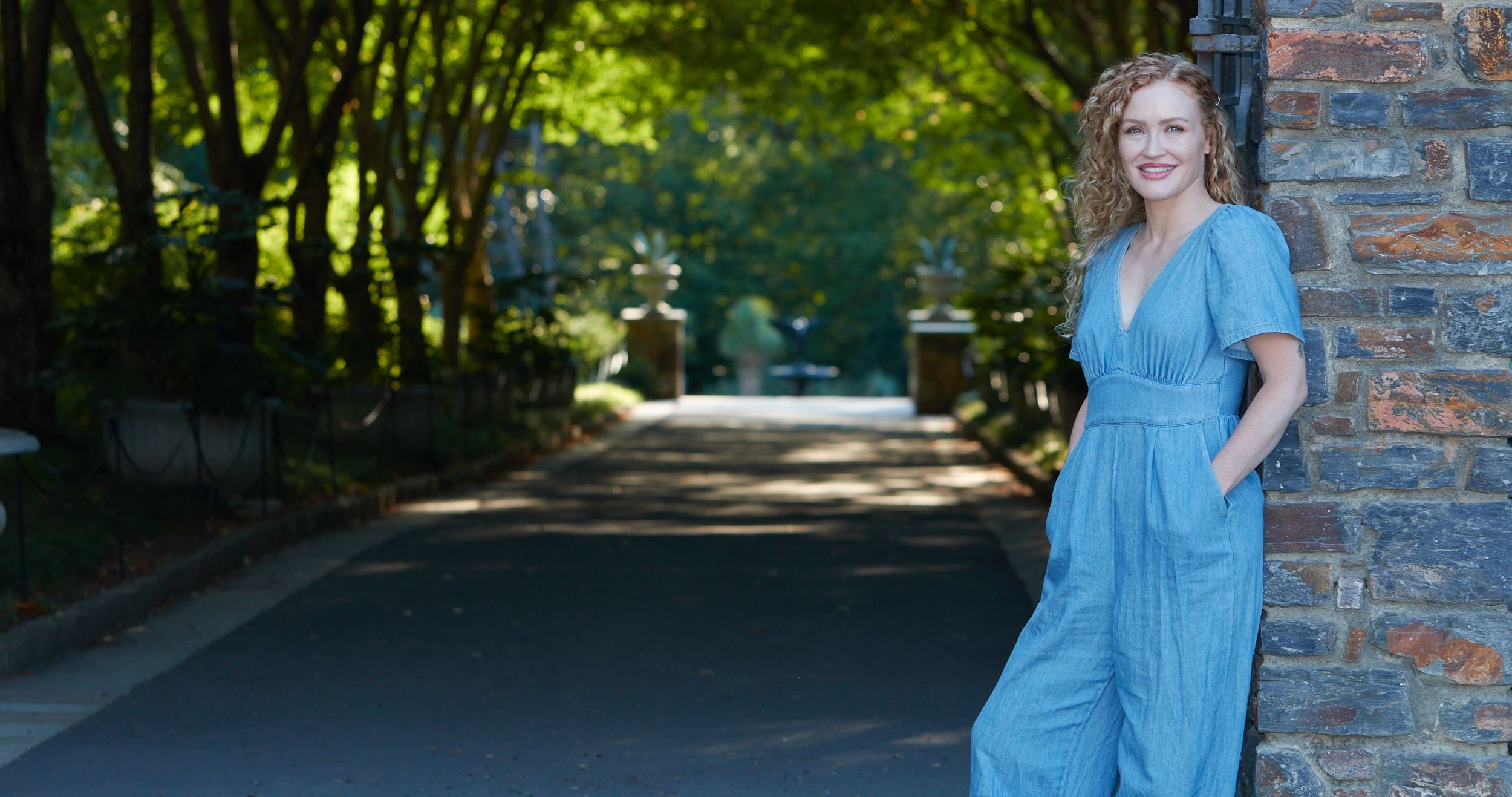 Carrie Davidson smiling beside the stone gothic gate on a tree-lined path