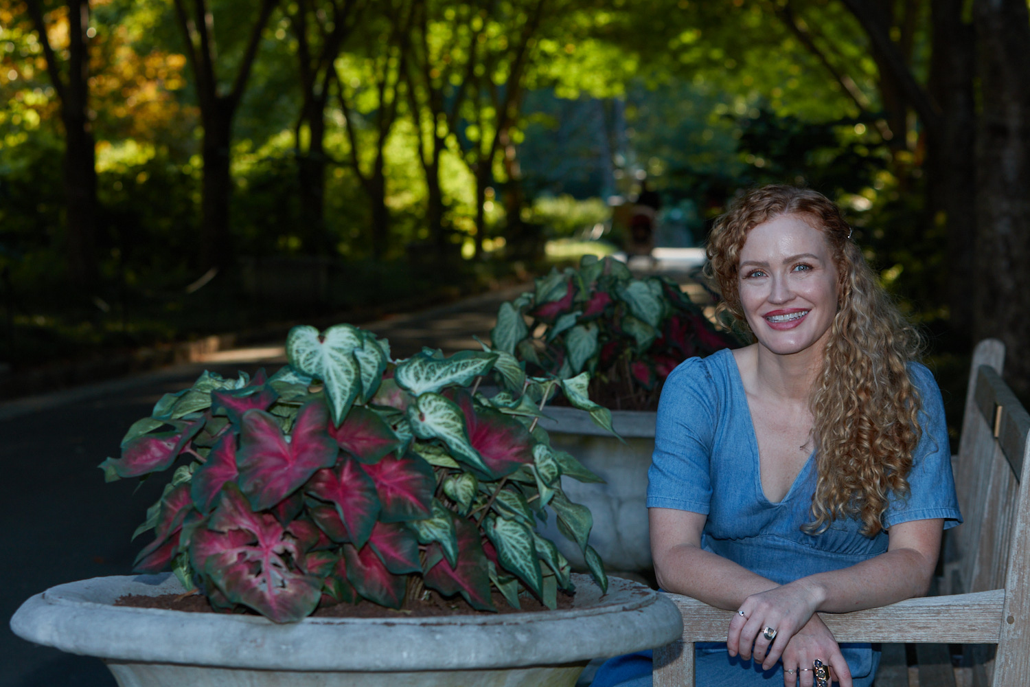 Carrie Davidson laughing on a garden bench beside a planter of pink caladiums