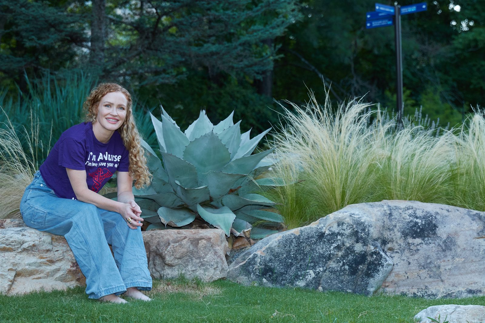 Carrie Davidson in a purple I'm A Nurse t-shirt, sitting barefoot on a garden wall