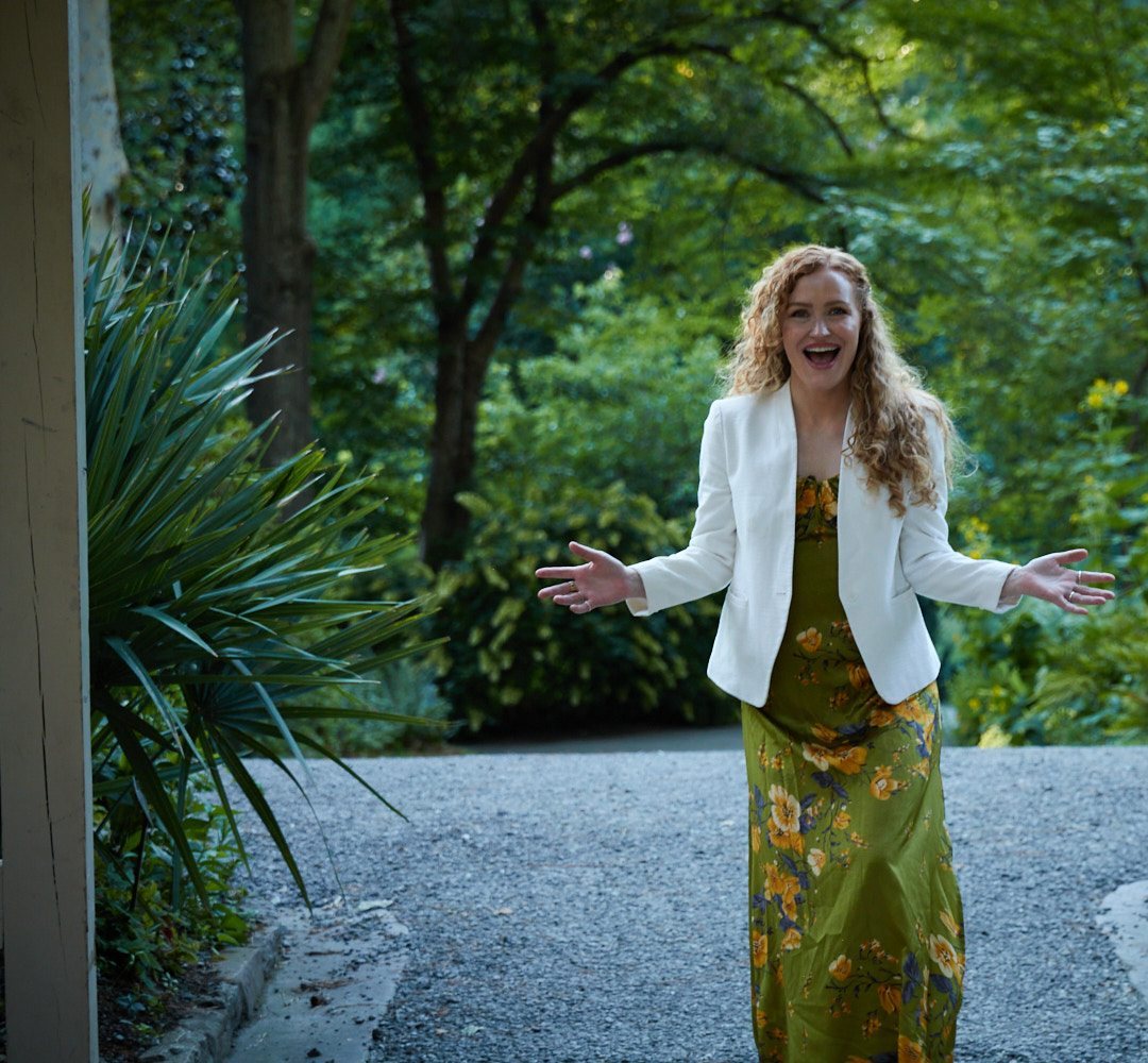 Carrie Davidson laughing with open arms at a garden doorway