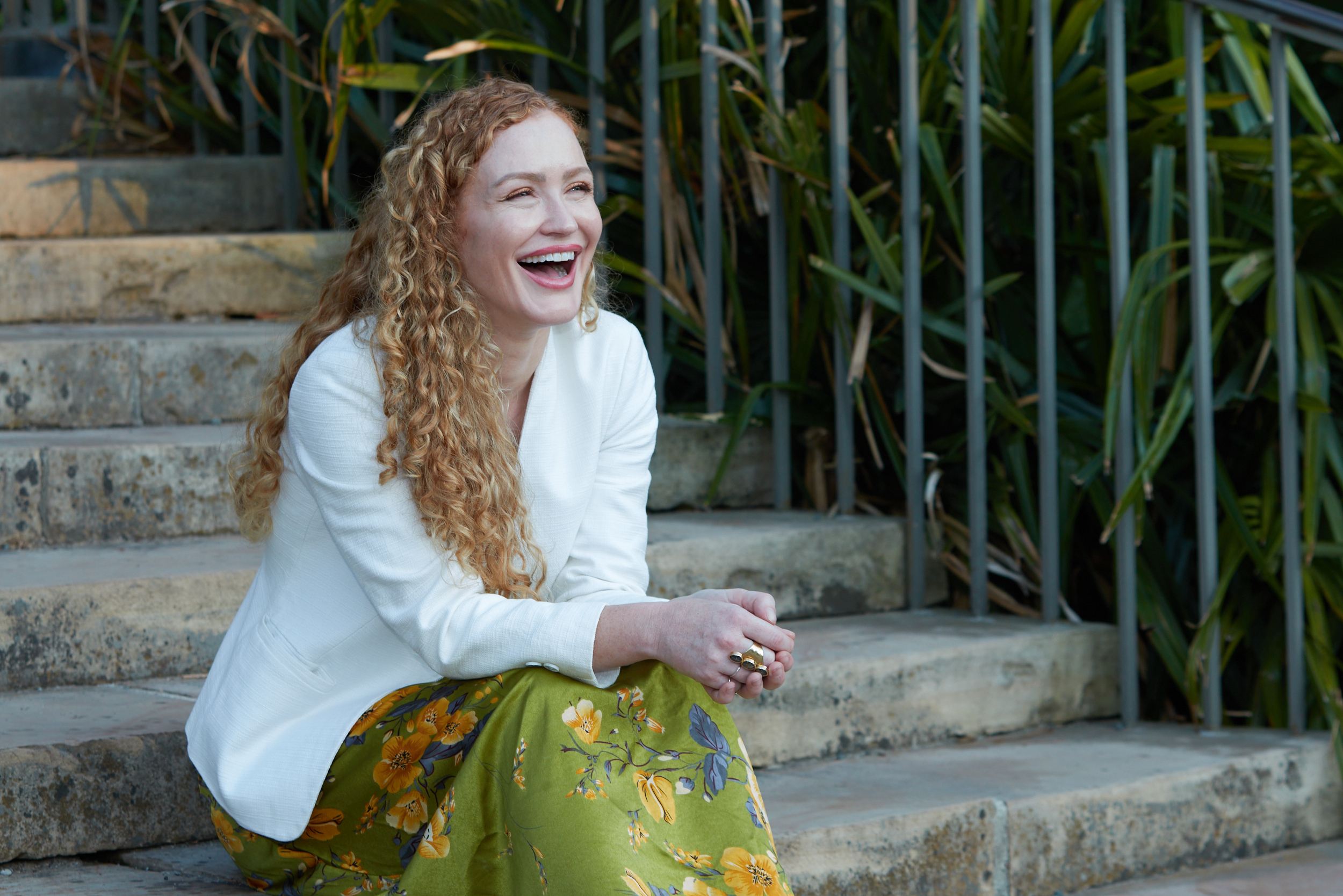 Carrie Davidson laughing on the stone steps in a white blazer