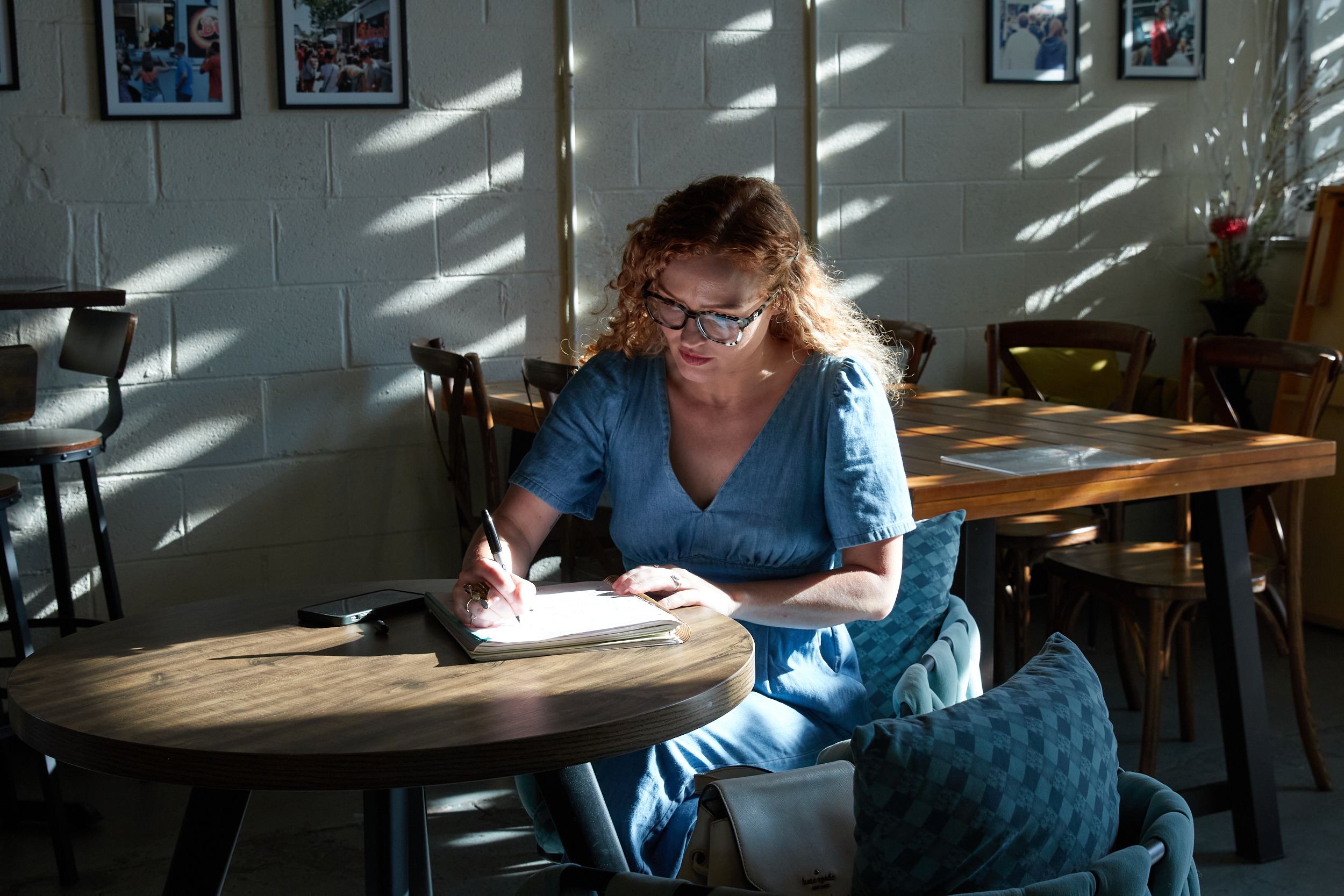 Carrie Davidson writing in a notebook at a sunlit cafe table